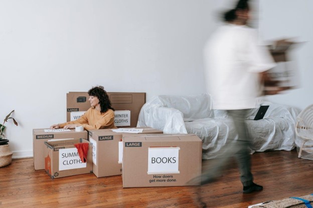 A woman labeling cardboard boxes while a man is passing by