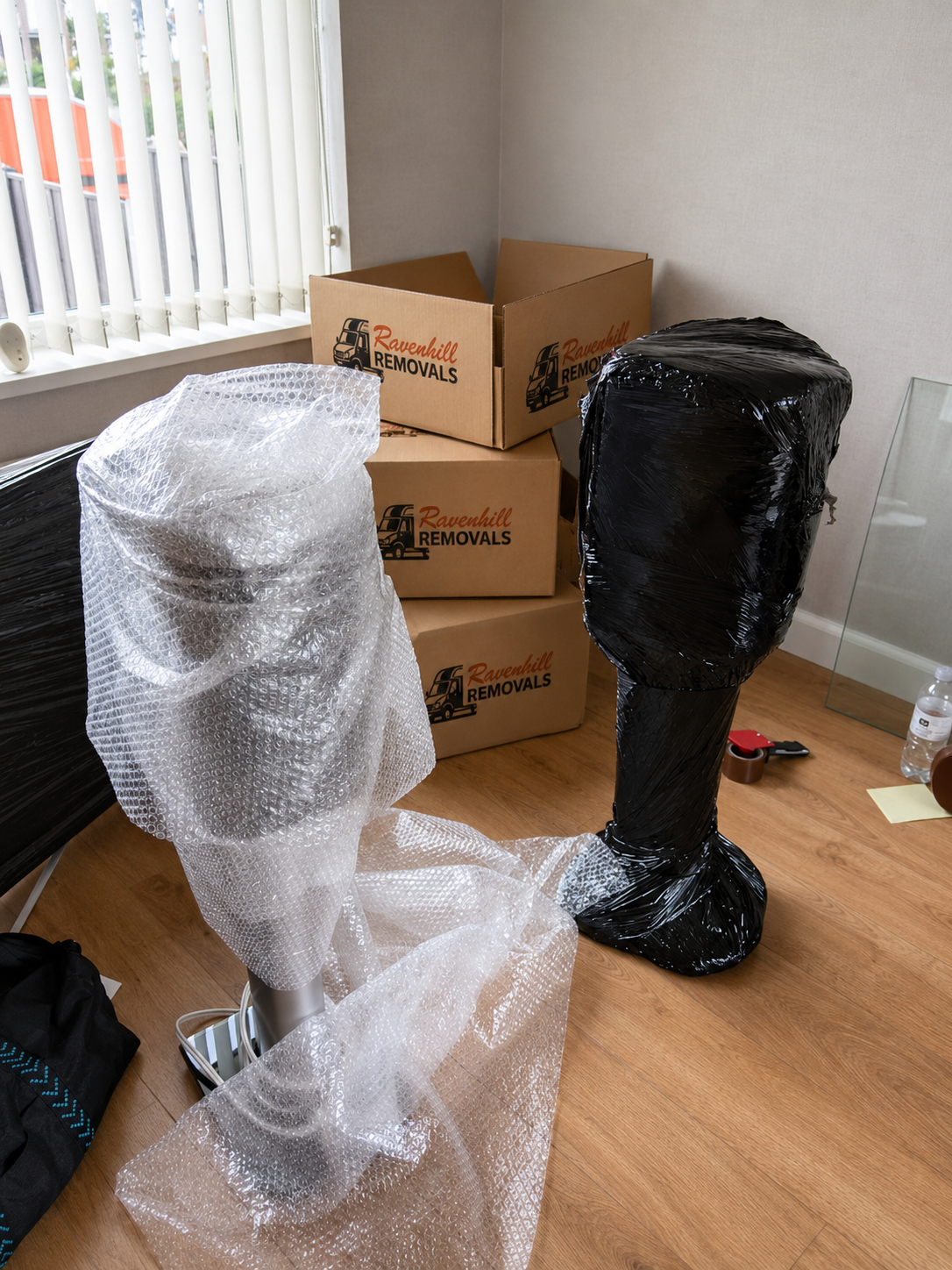 Speakers protected with bubble wrap and stretch wrap ready for a house move, with Ravenhill Removals moving boxes in the background
