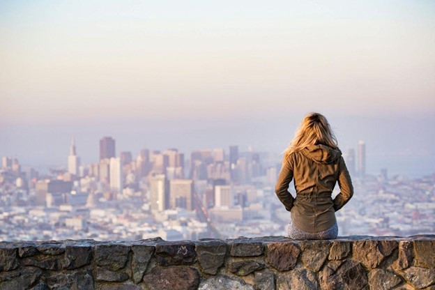 Why Researching the Destination Country Matters in Scam Prevention Person sitting on a viewpoint overlooking a large city skyline, reflecting on travel planning and why researching the destination country matters before moving abroad.