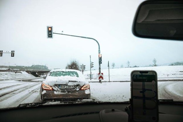 snowy road intersection with a car stopped at a red traffic light